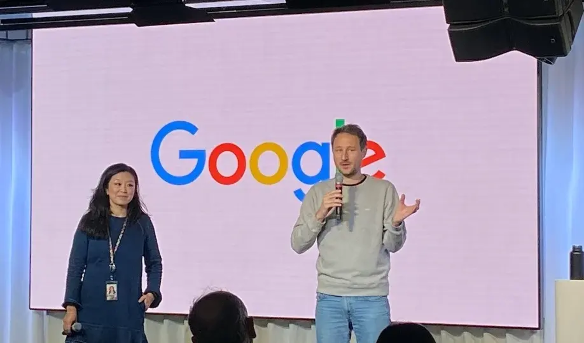 Two presenters on stage with a large Google logo backdrop.