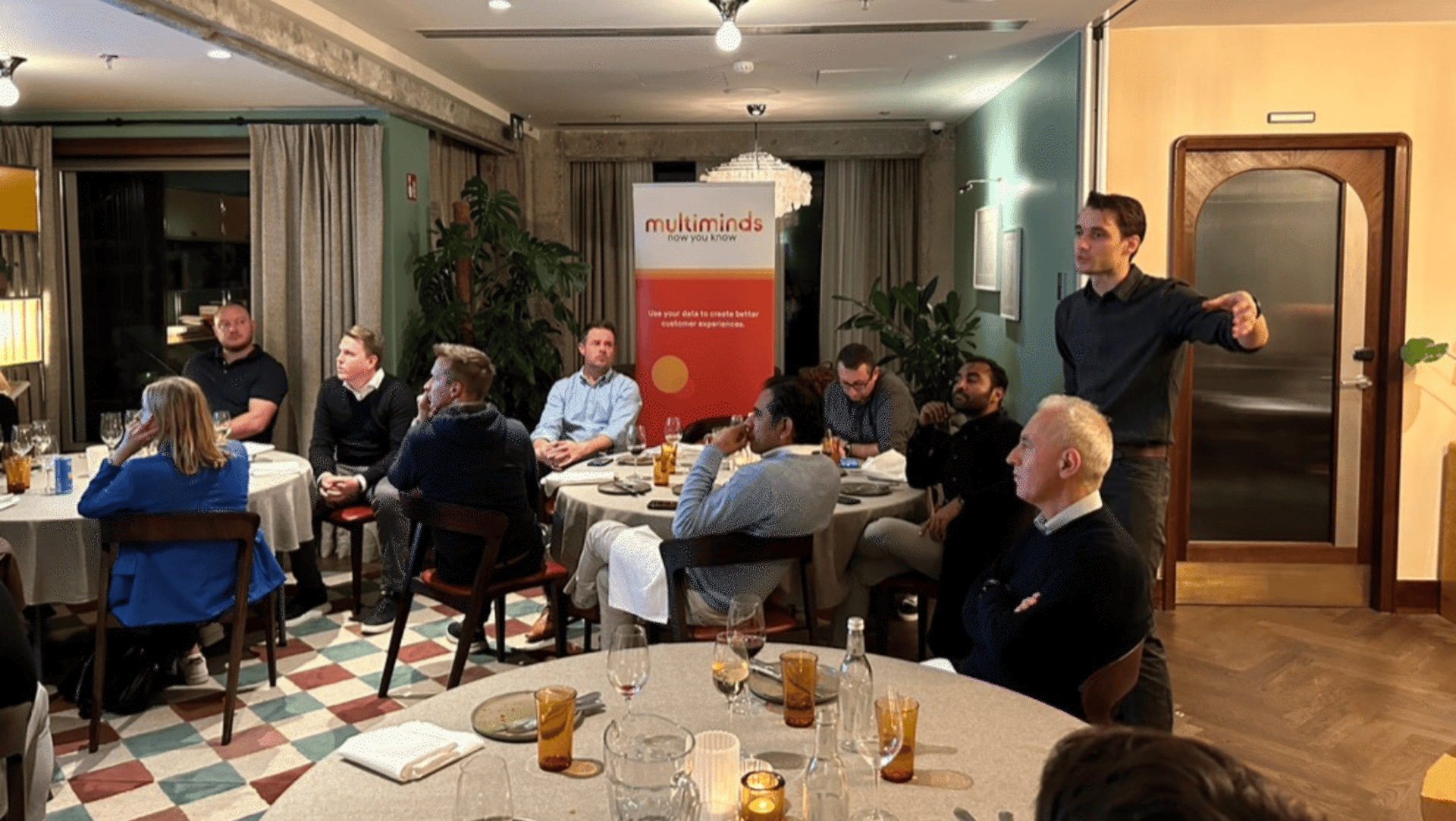 Multiminds event with attendees seated at tables and a speaker presenting.