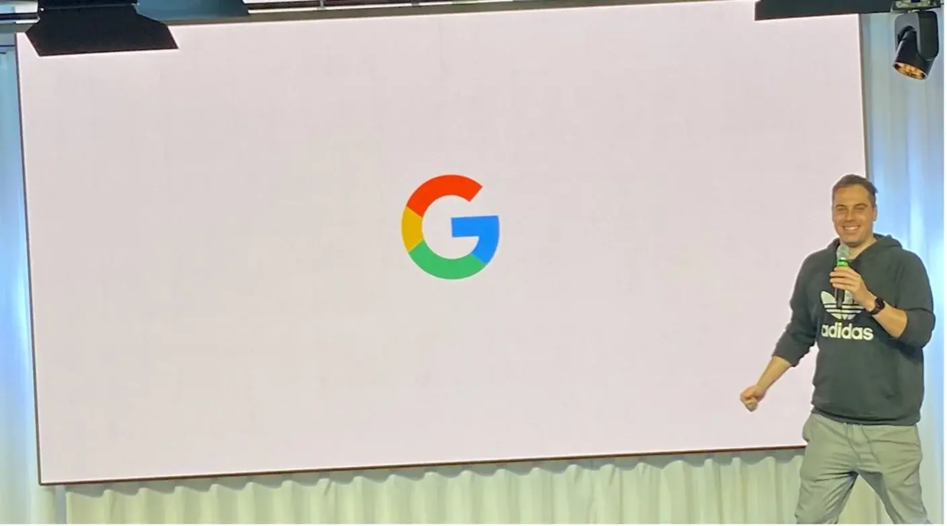 Man in Adidas hoodie presenting in front of a white screen with the colorful Google G logo.