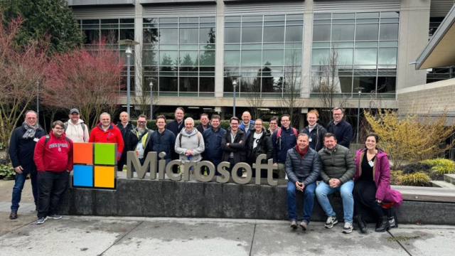 Large group of people posing in front of the Microsoft logo and building.